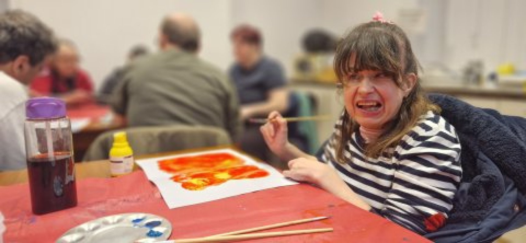 Smiling woman in a striped totting beside hernge and red painting