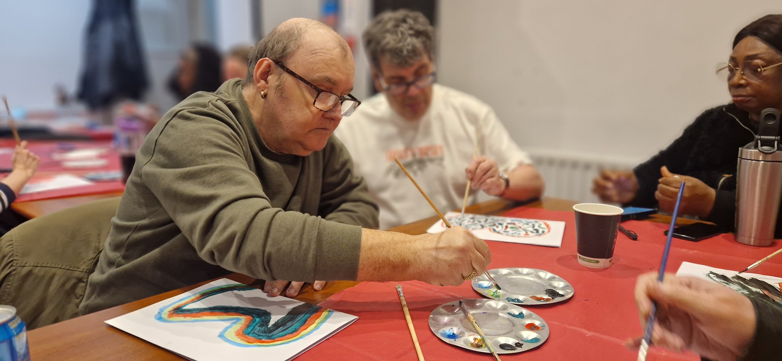 Man painting a colourful butterfly picture while other art group members sit nearby