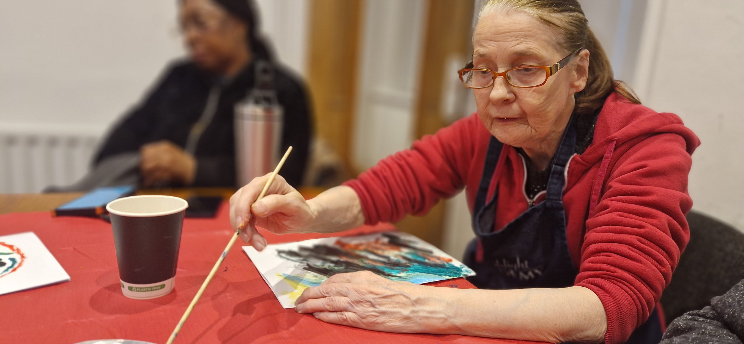 woman in a red fleece painting a colourful picture at the art table