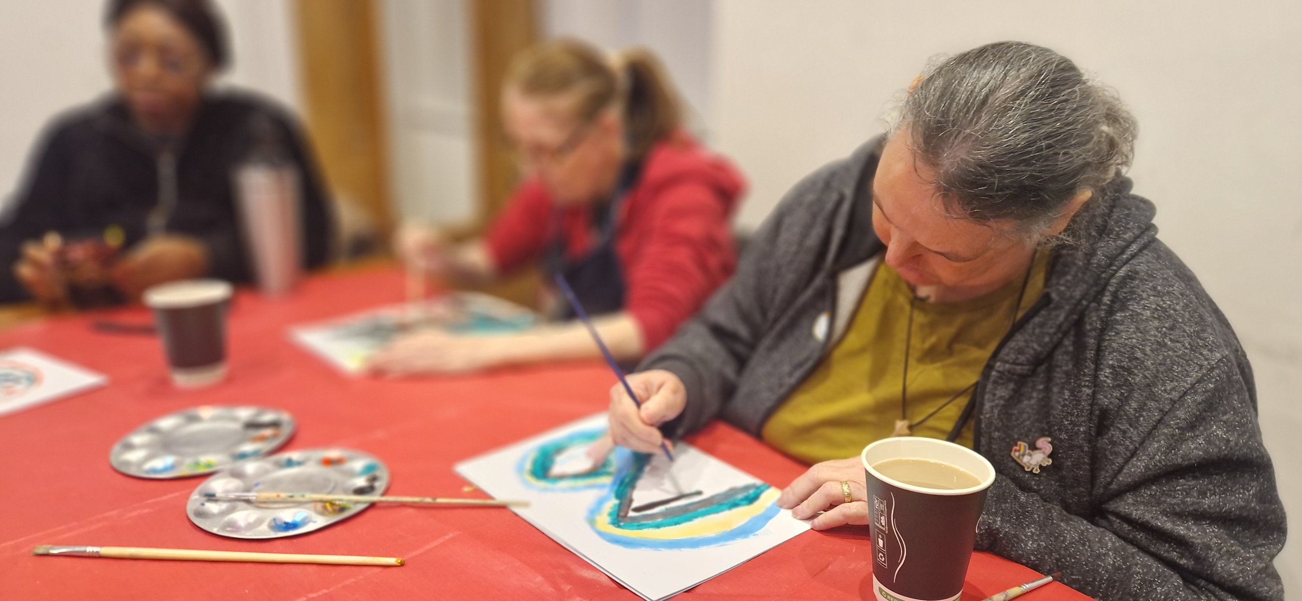 Women concentrating as she paints a blue and green butterfly shaped picture at a red table