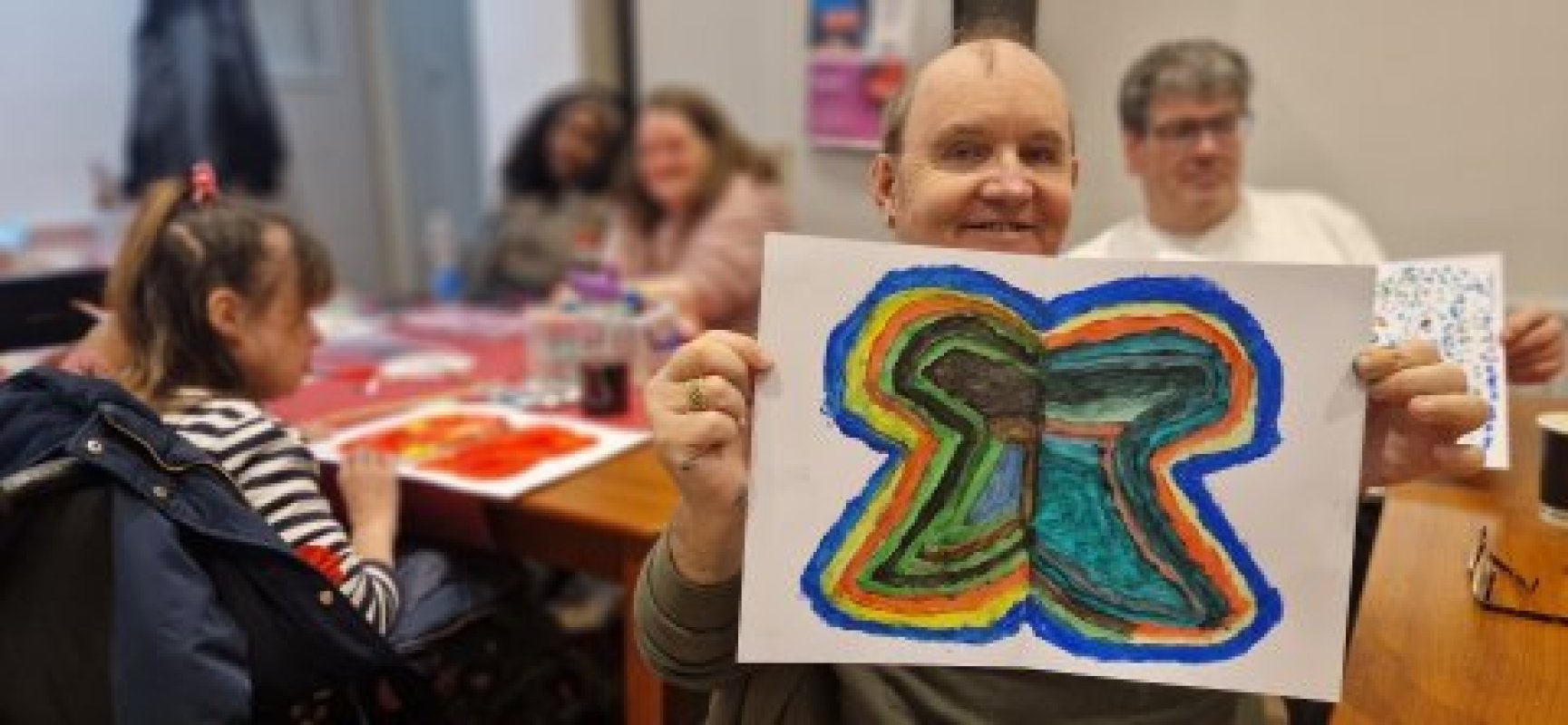 Smiling man hold a rainbow  butterfly painting at the art group