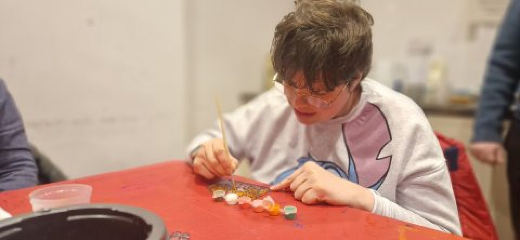 Person with glasses painting some glass at a red table