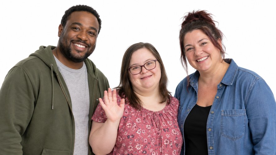 Three people: a Black man, a girl wearing a pink flowery top, and a woman on the right wearing a blue denim shirt.
