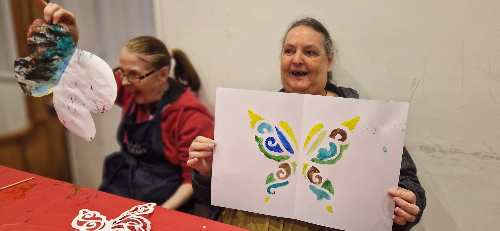 A womwn holding a print of a butterfly and someone next to her is flapping her butterfly she made in the air