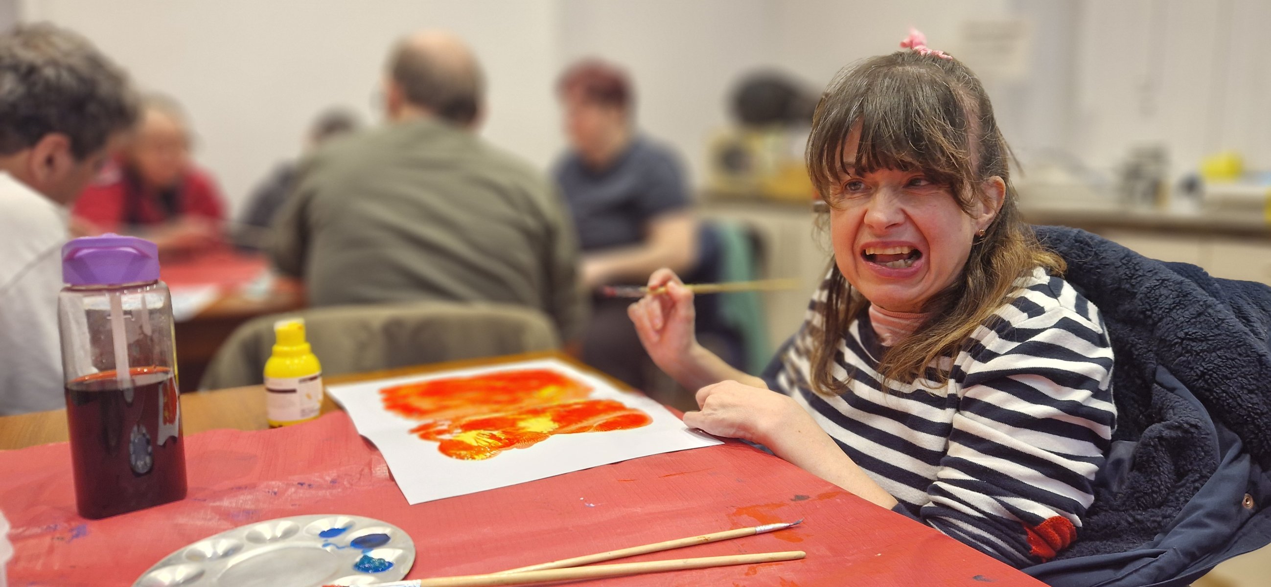 Smiling woman in a striped totting beside hernge and red painting