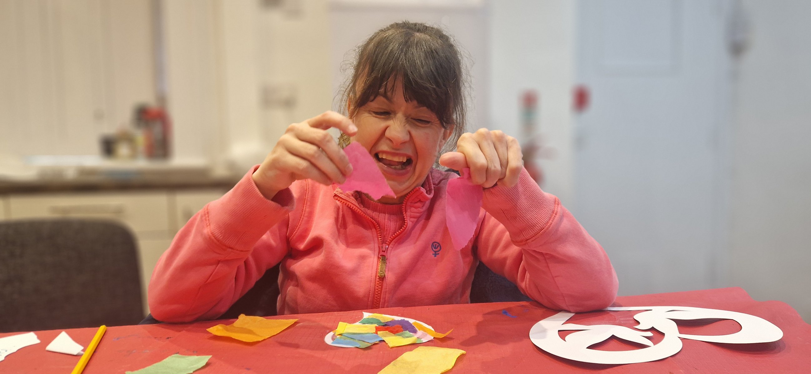 Woman smiling as holds up a colourful butterfly painting at the table
